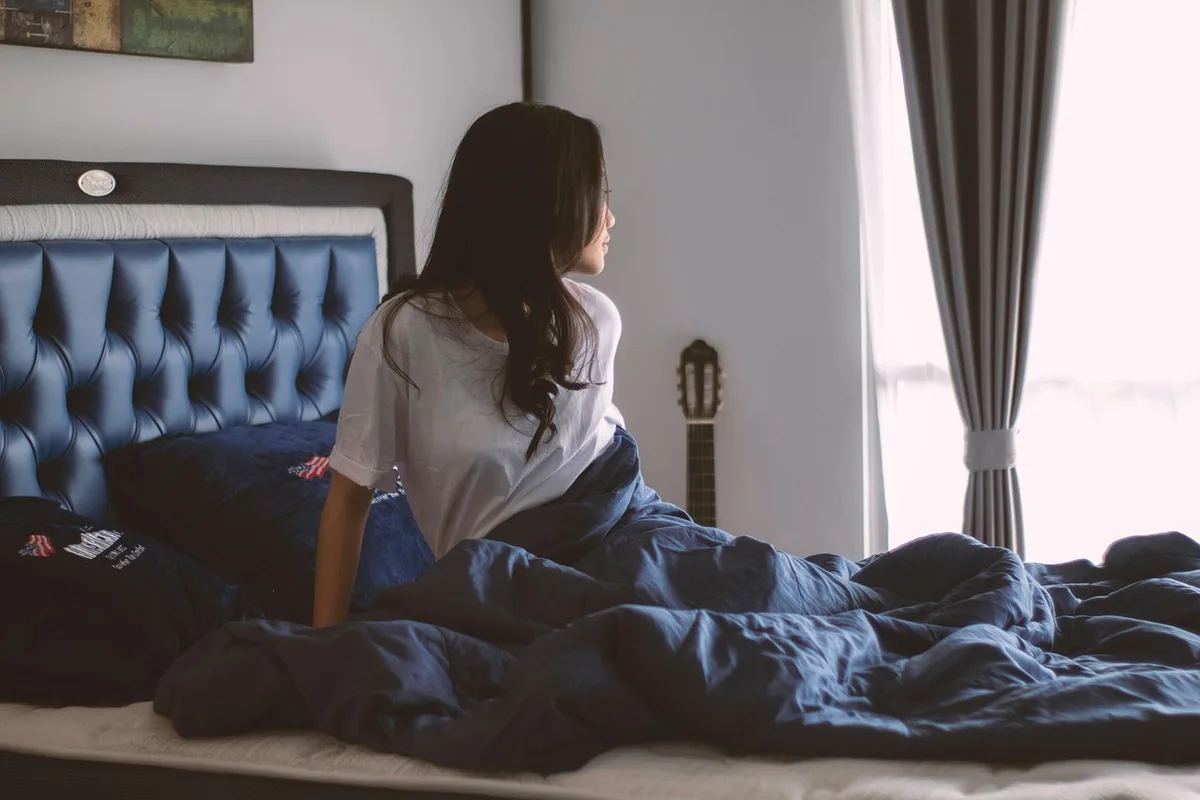 Coin de chambre épuré avec matelas, textiles pliés et vapeur à la fenêtre